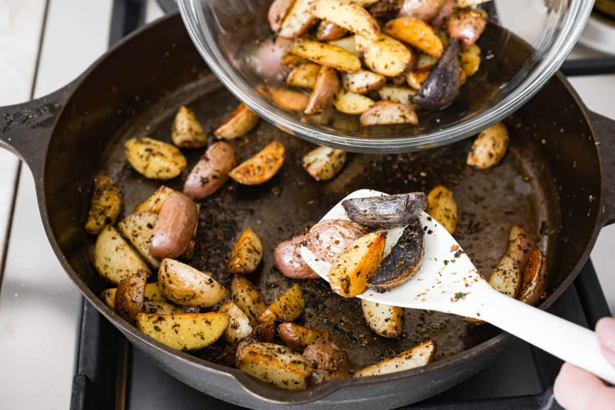 This sausage and potato skillet recipe is meant to be a simple one skillet meal! It has tender baby potatoes, smoked sausage, peppers, and delicious seasonings that take it over the top. It's hearty, satisfying and loaded with flavor! Third photo of the potatoes being removed from the skillet.