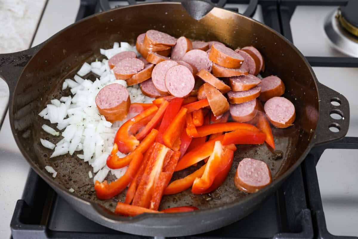 This sausage and potato skillet recipe is meant to be a simple one skillet meal! It has tender baby potatoes, smoked sausage, peppers, and delicious seasonings that take it over the top. It's hearty, satisfying and loaded with flavor! Fourth photo of the sausage, peppers, and onions cooking.