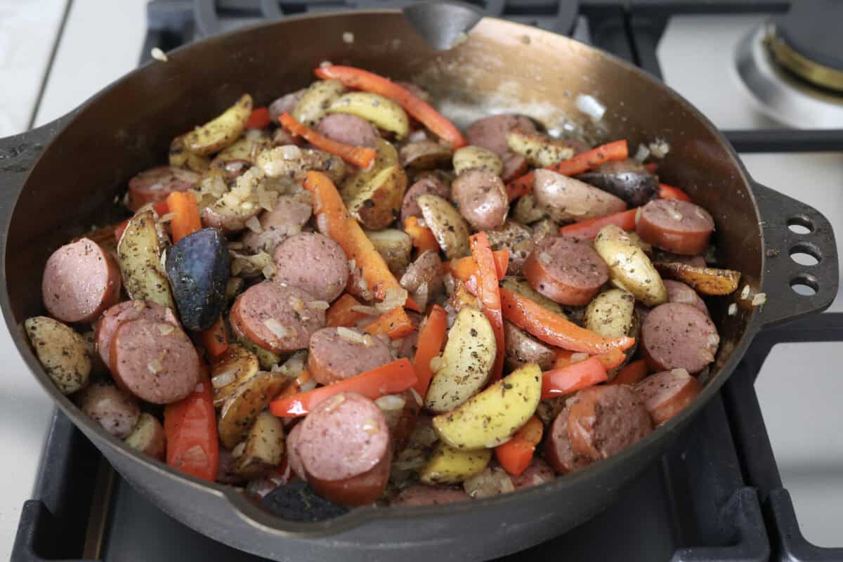 This sausage and potato skillet recipe is meant to be a simple one skillet meal! It has tender baby potatoes, smoked sausage, peppers, and delicious seasonings that take it over the top. It's hearty, satisfying and loaded with flavor! Fifth photo of the sausage and potato skillet heating through on the stove.