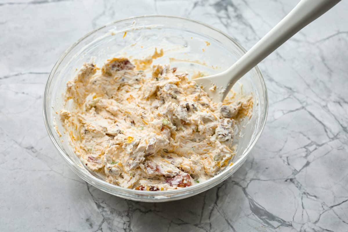 Million Dollar Chicken features juicy baked chicken topped with a creamy, cheesy layer that’s bursting with flavor. The crispy bacon and crunchy almonds really take this to the next level. Enjoy with rice, pasta, vegetables, or any of your favorite sides! Overhead shot of cream cheese topping mixture in a glass bowl.
