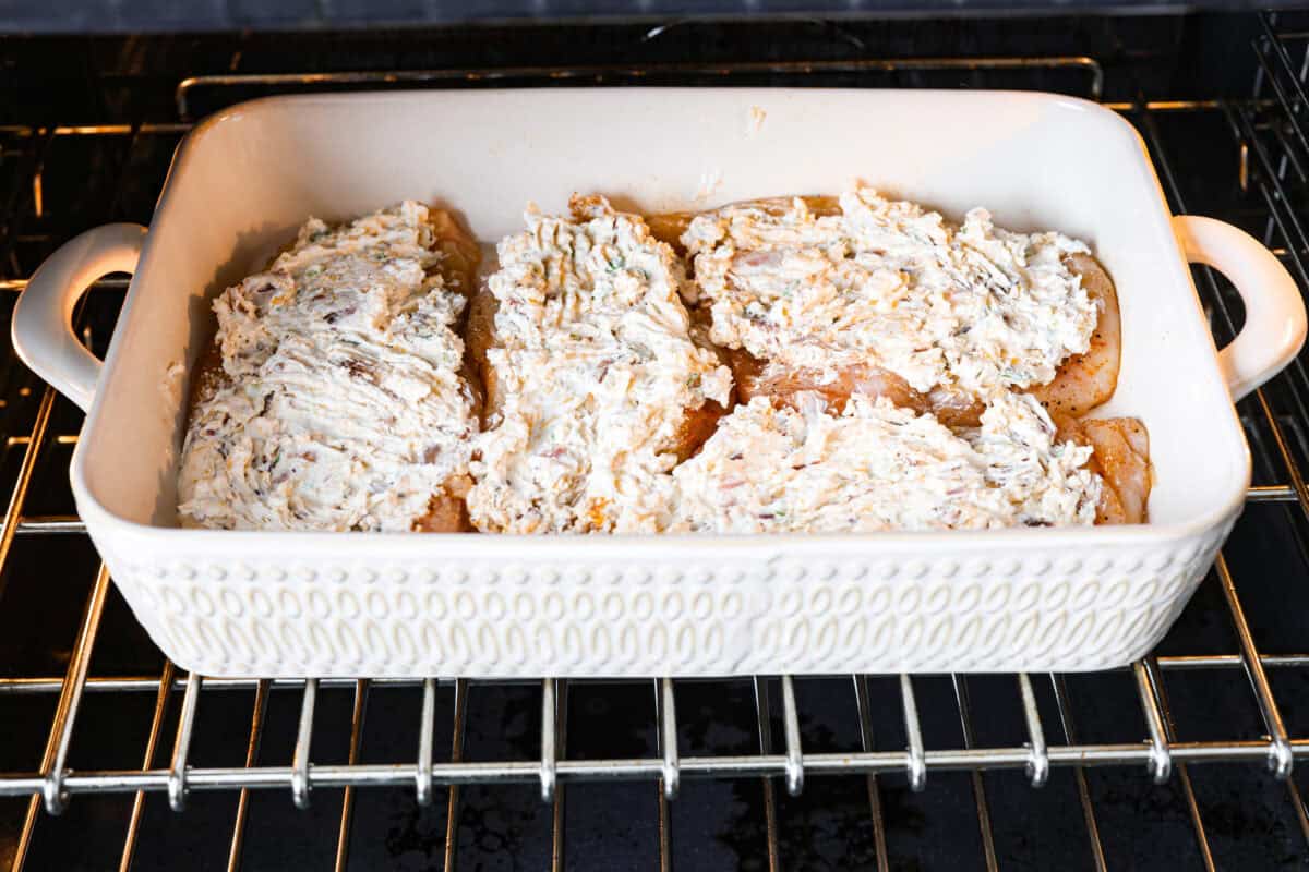 Million Dollar Chicken features juicy baked chicken topped with a creamy, cheesy layer that’s bursting with flavor. The crispy bacon and crunchy almonds really take this to the next level. Enjoy with rice, pasta, vegetables, or any of your favorite sides! Angle shot of topped chicken breasts in baking dish in the oven.