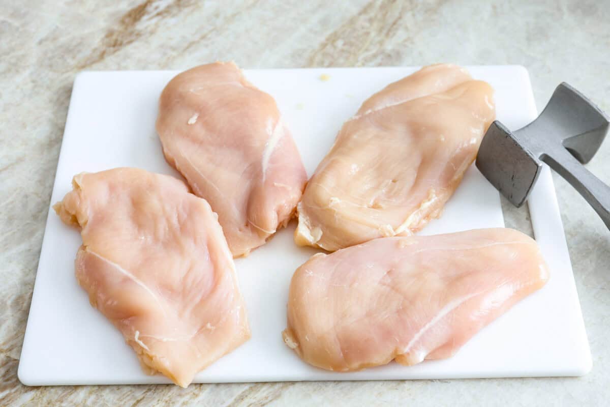Skillet chicken cordon bleu is one of those recipes my whole family loves. You can't beat the creamy sauce, crispy chicken, and smokey ham, all covered in melty Swiss cheese. Overhead shot of chicken breasts on a cutting board with meat tenderizer next to them.