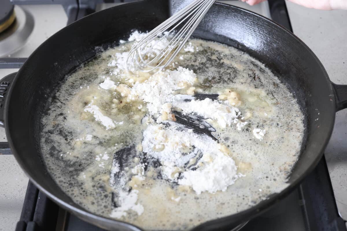 Skillet chicken cordon bleu is one of those recipes my whole family loves. You can't beat the creamy sauce, crispy chicken, and smokey ham, all covered in melty Swiss cheese. Angle shot of someone whisking the flour into the melted butter in a skillet.