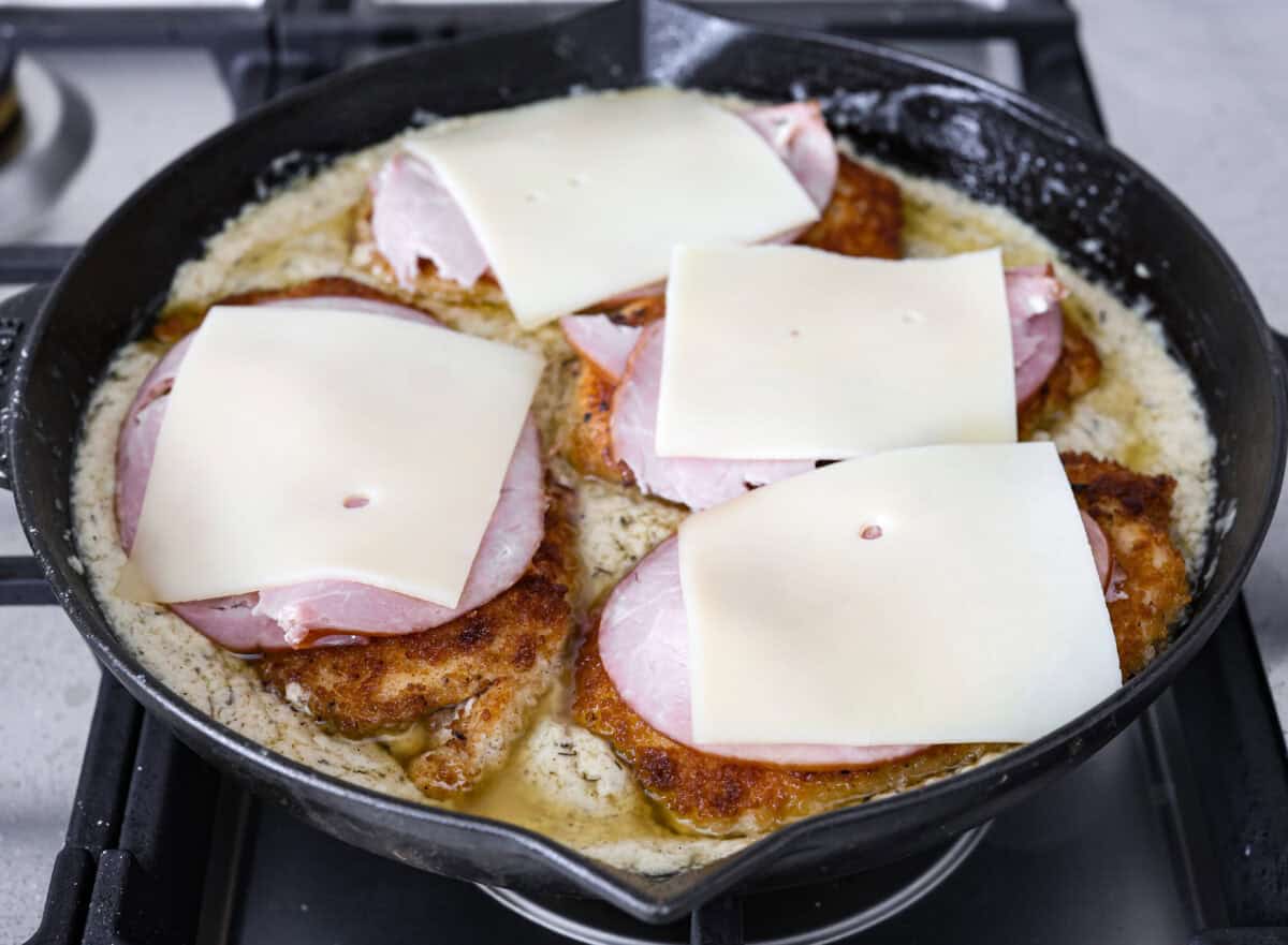 Skillet chicken cordon bleu is one of those recipes my whole family loves. You can't beat the creamy sauce, crispy chicken, and smokey ham, all covered in melty Swiss cheese. Angle shot of the crispy chicken breasts covered in ham and cheese in the skillet with the sauce.