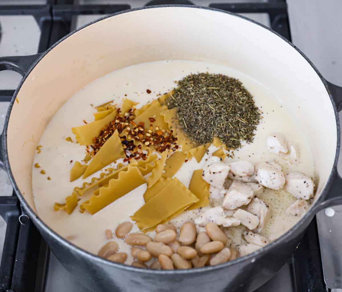 Comforting White Lasagna Soup is warm, creamy, and packed with rich flavors. With its hearty mix of chicken, noodles, white beans, and cheese, it’s a guaranteed crowd-pleaser. Deconstructed white lasagna in a satisfying soup! Overhead shot of beans, noodles, seasoning and chicken added to the pot with the soup base.