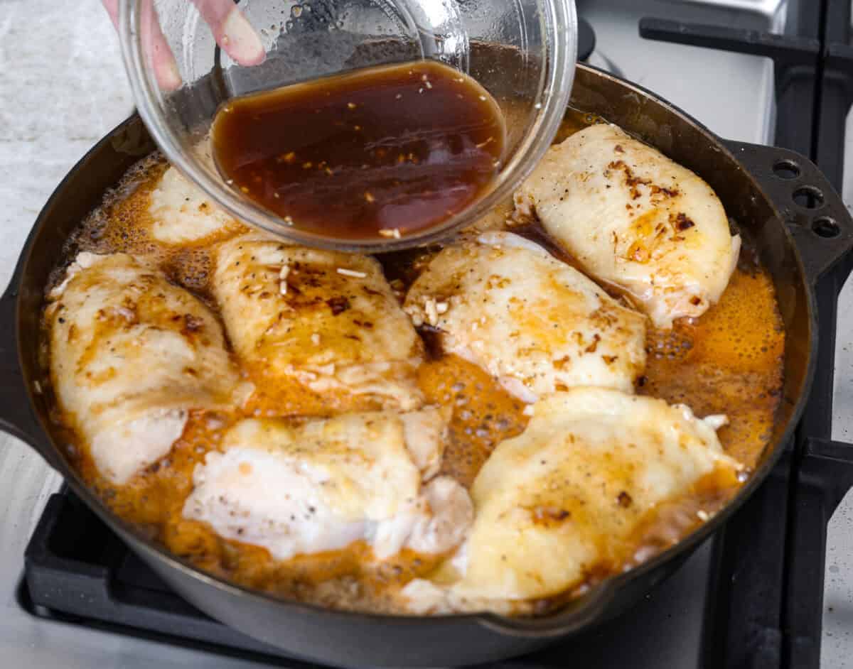 This incredibly tasty Coca-Cola chicken thigh recipe can be on the table in 40 minutes. The succulent sauce is a combination of savory soy sauce, Worcestershire, garlic, ketchup, and, of course, Coca-Cola. You've never had more flavorful chicken thighs than these! Angle shot of someone pouring sauce over chicken thighs in skillet.