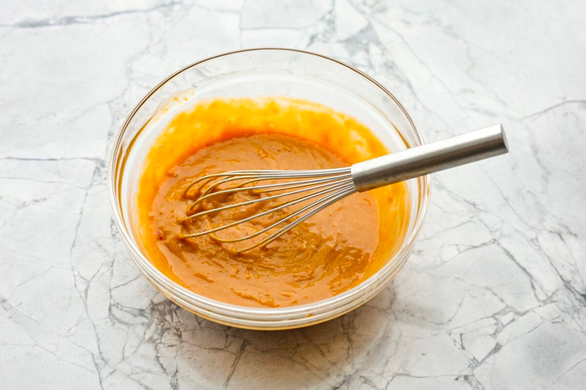 Thai peanut dressing is perfect for drizzling over fresh chopped salads or dipping veggies. It's a creamy mix of peanut butter, soy sauce, lime juice, and sweet chili sauce with a touch of garlic and ginger. Itโs nutty and tangy, with the perfect amount of spice. Angle shot of dressing ingredients in a glass bowl with a whisk.