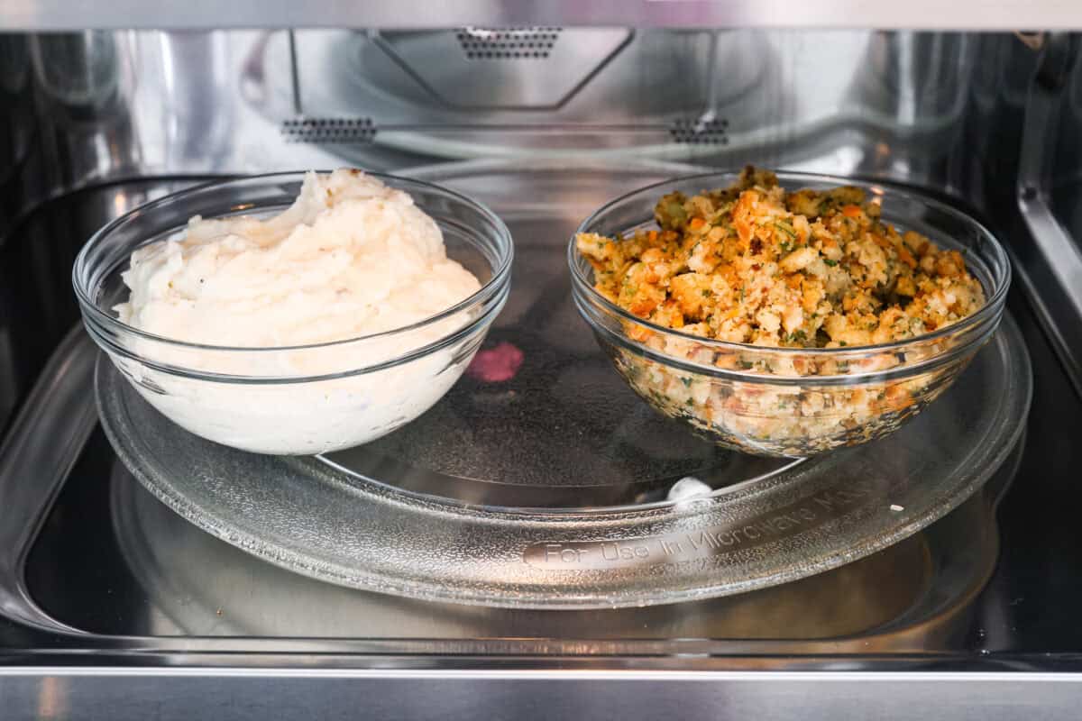 Turkey Stuffing Balls capture the taste of Thanksgiving in a single bite! Made with tender turkey, flavorful stuffing, and mashed potatoes. Theyโre rolled into perfectly poppable bites and served with rich gravy for dipping. Side shot of a bowl of mashed potatoes next to a bowl of stuffing in a microwave.