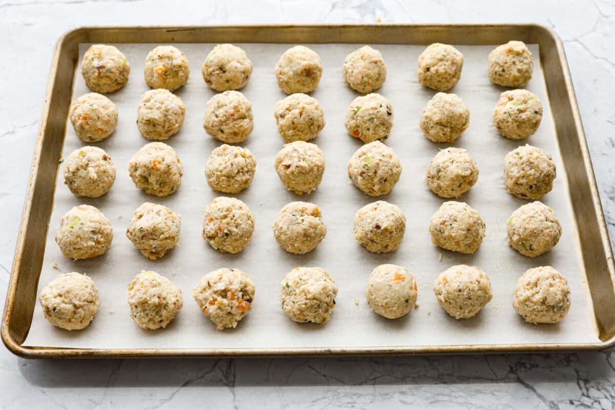 Turkey Stuffing Balls capture the taste of Thanksgiving in a single bite! Made with tender turkey, flavorful stuffing, and mashed potatoes. Theyโre rolled into perfectly poppable bites and served with rich gravy for dipping. Angle shot of the balls evenly spaced on a cookie sheet.