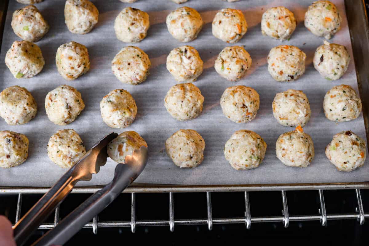 Turkey Stuffing Balls capture the taste of Thanksgiving in a single bite! Made with tender turkey, flavorful stuffing, and mashed potatoes. Theyโre rolled into perfectly poppable bites and served with rich gravy for dipping. Angle shot of someone flipping the balls in the oven.