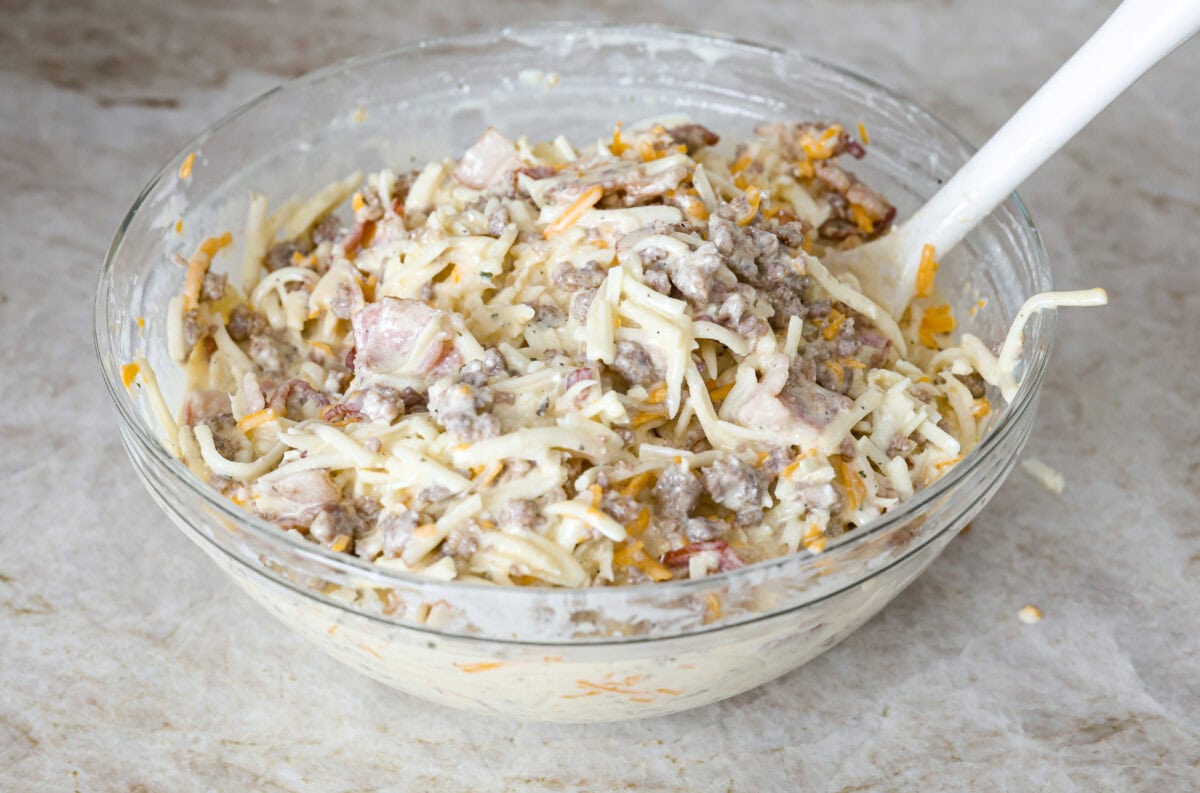 Crack breakfast casserole gets its name for a reason. It is bursting with delicious flavors you won't want to stop eating! It's packed with layers of shredded potatoes, crispy bacon, sausage, and smooth cream cheese, topped with a layer of crispy cheese. Angle shot of the egg and cream cheese mixture mixed in with the hash browns and meats.
