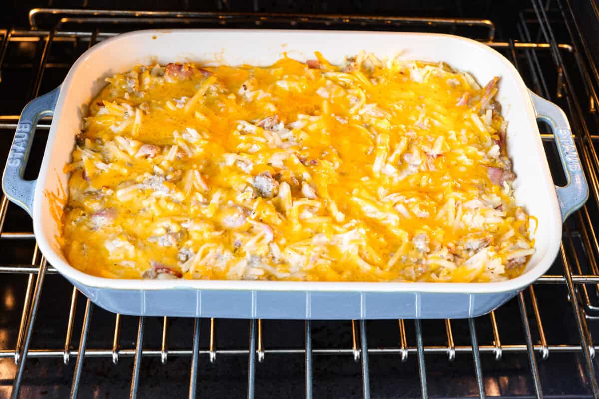 Crack breakfast casserole gets its name for a reason. It is bursting with delicious flavors you won't want to stop eating! It's packed with layers of shredded potatoes, crispy bacon, sausage, and smooth cream cheese, topped with a layer of crispy cheese. Angle shot of crack breakfast casserole being baked in the oven.