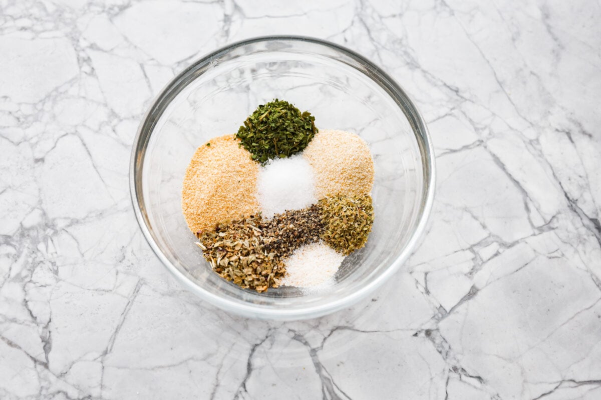 Homemade garlic herb seasoning is a great mix to have on hand. It has multiple uses, is full of flavor, and is adjustable to suit your taste preferences. It has the perfect mix of herbaceous dried herbs, garlic, onion powder, salt, and fresh cracked pepper. Overhead shot of the herbs and spices in a glass bowl.