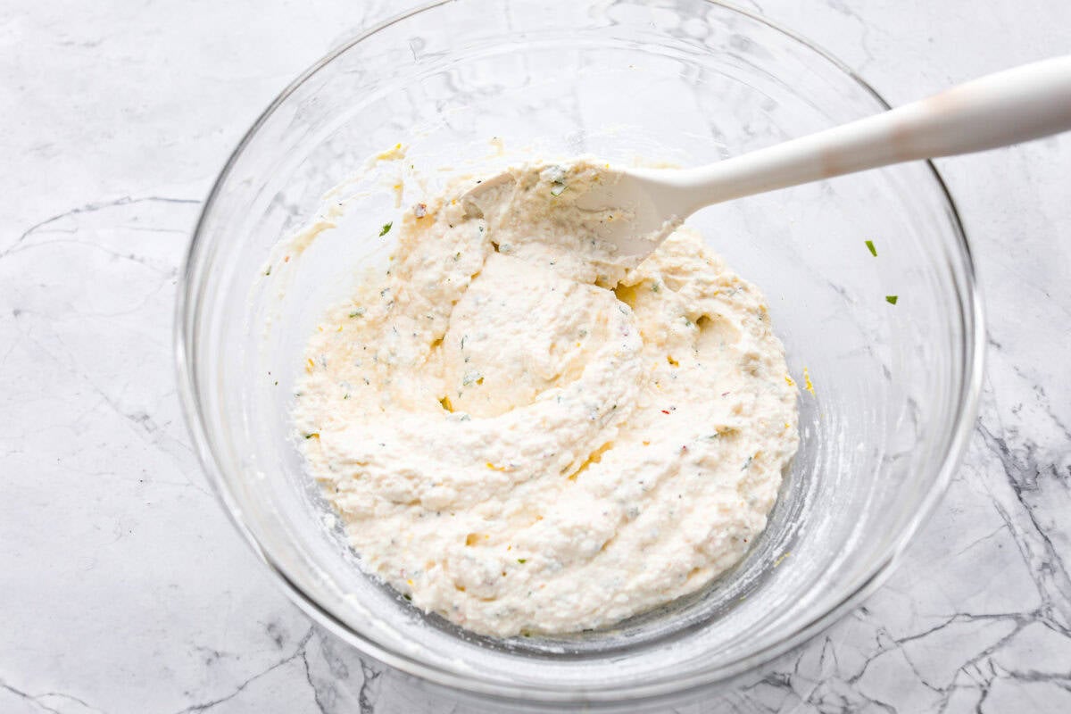 Irresistible Baked Ricotta Dip is the perfect party appetizer! It takes just minutes to combine creamy ricotta cheese with parmesan, fresh herbs, and lemon zest. Then, bake until bubbly and delicious, and get ready for an explosion of flavor! Overhead shot of ingredients stirred up in a glass bowl.