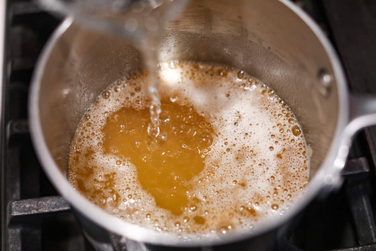 Browned Butter Sheet Cake is the perfect blend of moist, sweet, and irresistibly nutty. With the rich, caramel-like flavor of browned butter baked into every bite, this cake is a treat for anyone who loves a touch of warmth in their desserts. Overhead shot of someone pouring water into the browned butter.