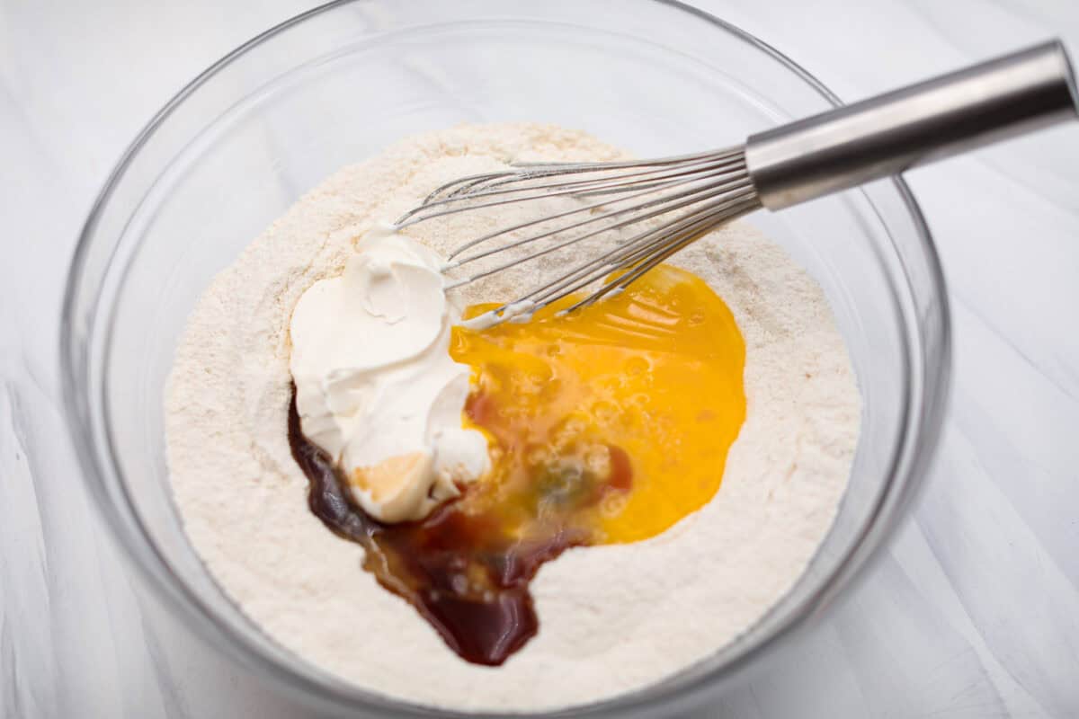 Browned Butter Sheet Cake is the perfect blend of moist, sweet, and irresistibly nutty. With the rich, caramel-like flavor of browned butter baked into every bite, this cake is a treat for anyone who loves a touch of warmth in their desserts. Overhead shot of sour cream, eggs, vanilla baking powder and salt being whisked in with the dry ingredients.
