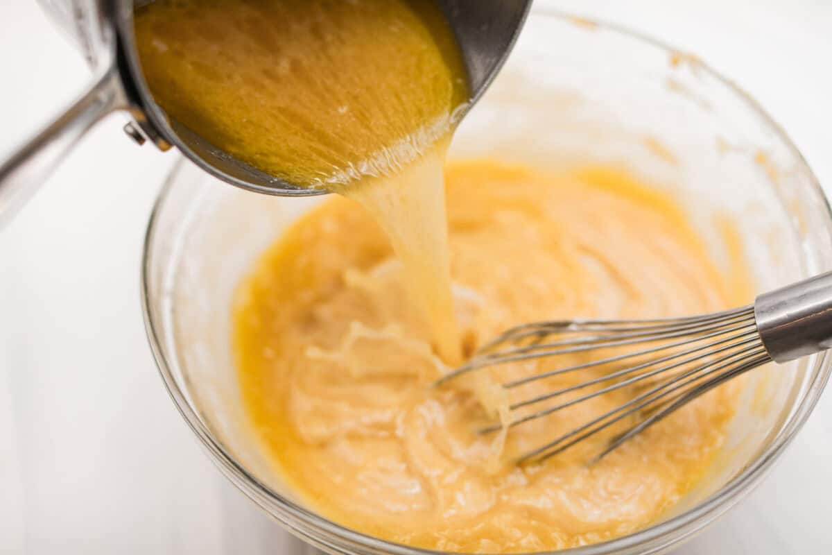 Browned Butter Sheet Cake is the perfect blend of moist, sweet, and irresistibly nutty. With the rich, caramel-like flavor of browned butter baked into every bite, this cake is a treat for anyone who loves a touch of warmth in their desserts. Angle shot of someone pouring the water and browned butter into the dry ingredients while whisking.