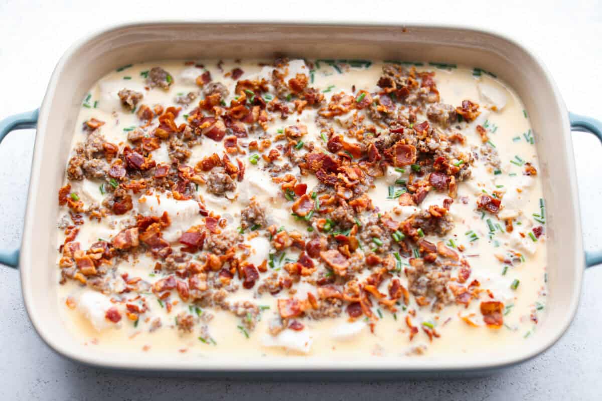 This bubble up breakfast casserole is simple to prepare and super flavorful! It's made with layers of biscuit, crispy bacon, savory sausage, fluffy eggs and melty cheese. Everyone will get out of bed and run to the breakfast table for this yummy dish! Overhead shot of meat and biscuit pieces covered in the egg mixture.