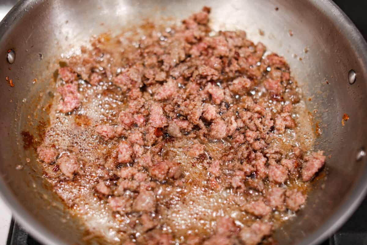 This bubble up breakfast casserole is simple to prepare and super flavorful! It's made with layers of biscuit, crispy bacon, savory sausage, fluffy eggs and melty cheese. Everyone will get out of bed and run to the breakfast table for this yummy dish! Overhead shot of the sausage being cooked in the bacon grease in a skillet.