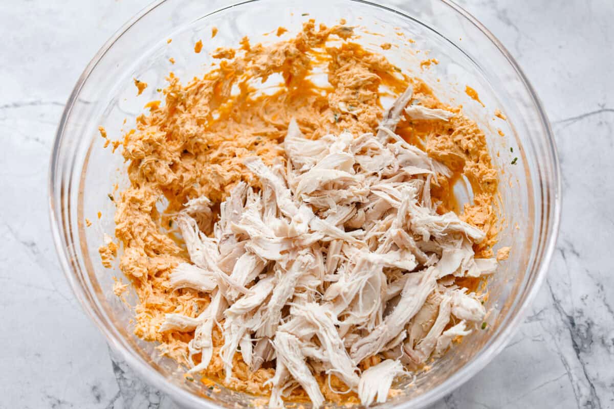 These zesty Buffalo Chicken Pinwheels are an easy snack or appetizer that everyone will devour! A creamy buffalo-flavored spread full of shredded chicken, seasonings, and cheeses all rolled inside of a soft tortilla. Slice into cute pinwheels and enjoy! Third photo of the shredded chicken added to the cream cheese mixture.