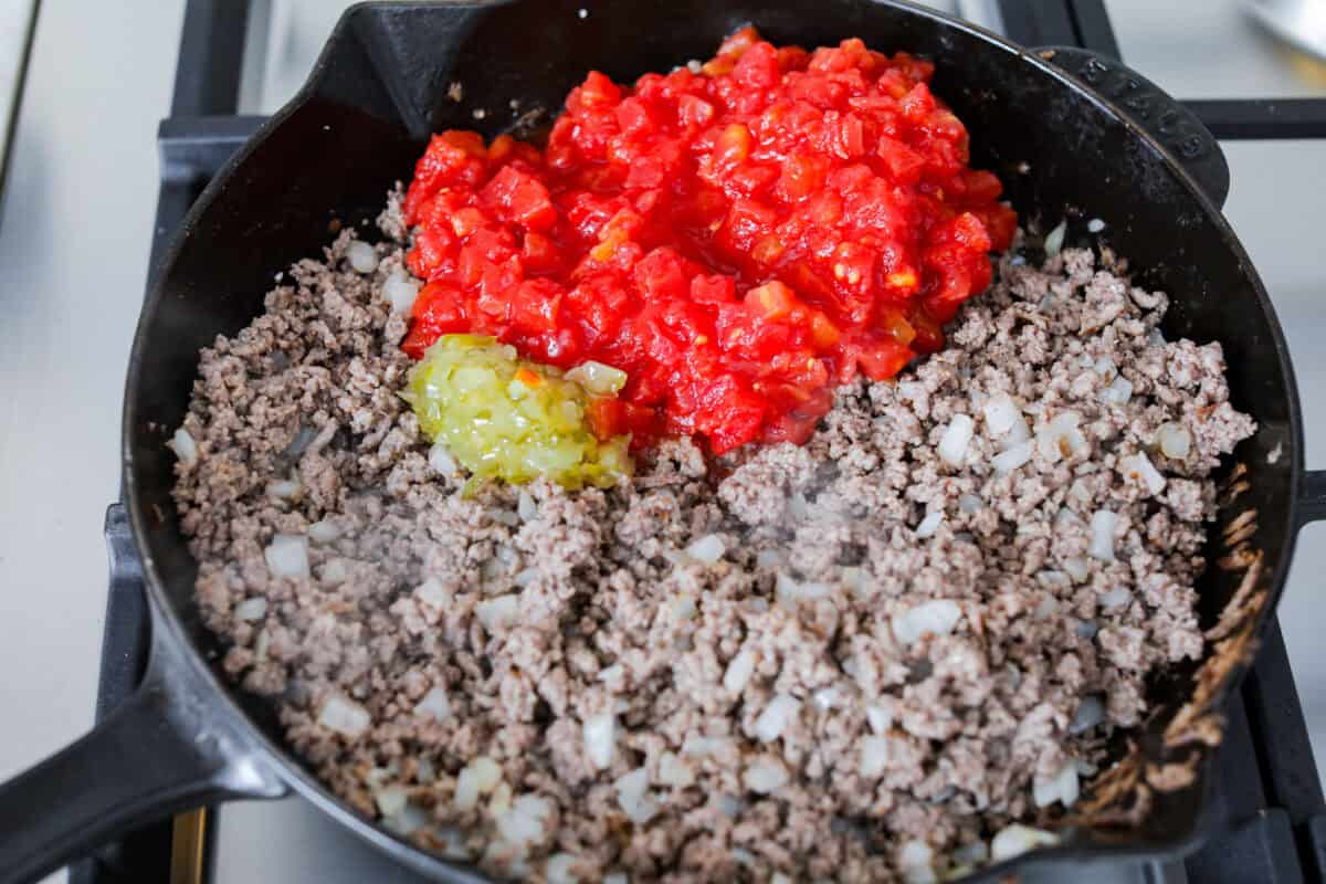 Cheeseburger dip is a crowd-pleasing appetizer for potlucks, parties, and get-togethers! This recipe takes delicious cheeseburger ingredients like beef, onion, tomato, relish, and cheese and turns them into a deliciously addicting snack! Overhead shot of browned beef with onions, tomatoes and relish.