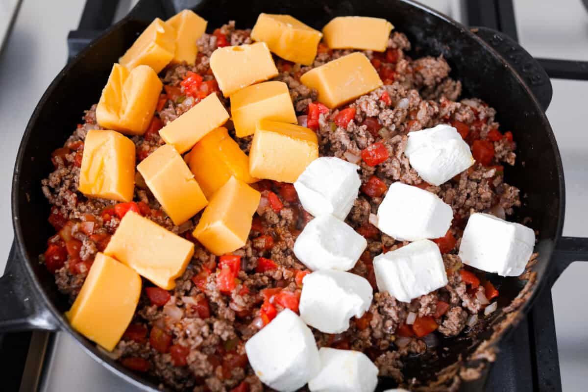 Cheeseburger dip is a crowd-pleasing appetizer for potlucks, parties, and get-togethers! This recipe takes delicious cheeseburger ingredients like beef, onion, tomato, relish, and cheese and turns them into a deliciously addicting snack! Overhead shot of beef mixture with Velveeta and cream cheese on top.