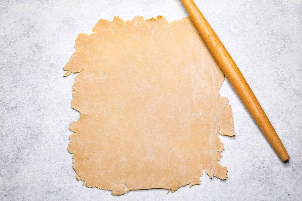 Cherry Slab Pie is an American classic made to serve a crowd! This recipe uses a tender, flaky crust that surrounds sweet, juicy cherry pie filling. It tastes incredibly delicious and is the perfect dessert for any time of year. Overhead shot of pie crust rolled into a rectangle with a rolling pin next to it.