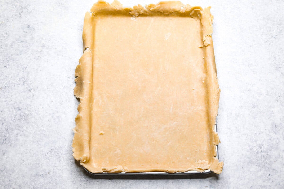 Cherry Slab Pie is an American classic made to serve a crowd! This recipe uses a tender, flaky crust that surrounds sweet, juicy cherry pie filling. It tastes incredibly delicious and is the perfect dessert for any time of year. Overhead shot of pie crust spread out in jelly roll pan.