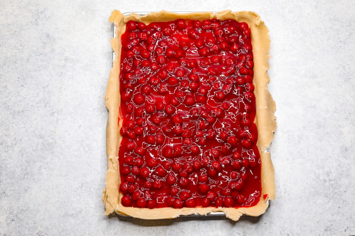 Cherry Slab Pie is an American classic made to serve a crowd! This recipe uses a tender, flaky crust that surrounds sweet, juicy cherry pie filling. It tastes incredibly delicious and is the perfect dessert for any time of year. Overhead shot of pie crust on sheet pan filled with cherry pie filling.