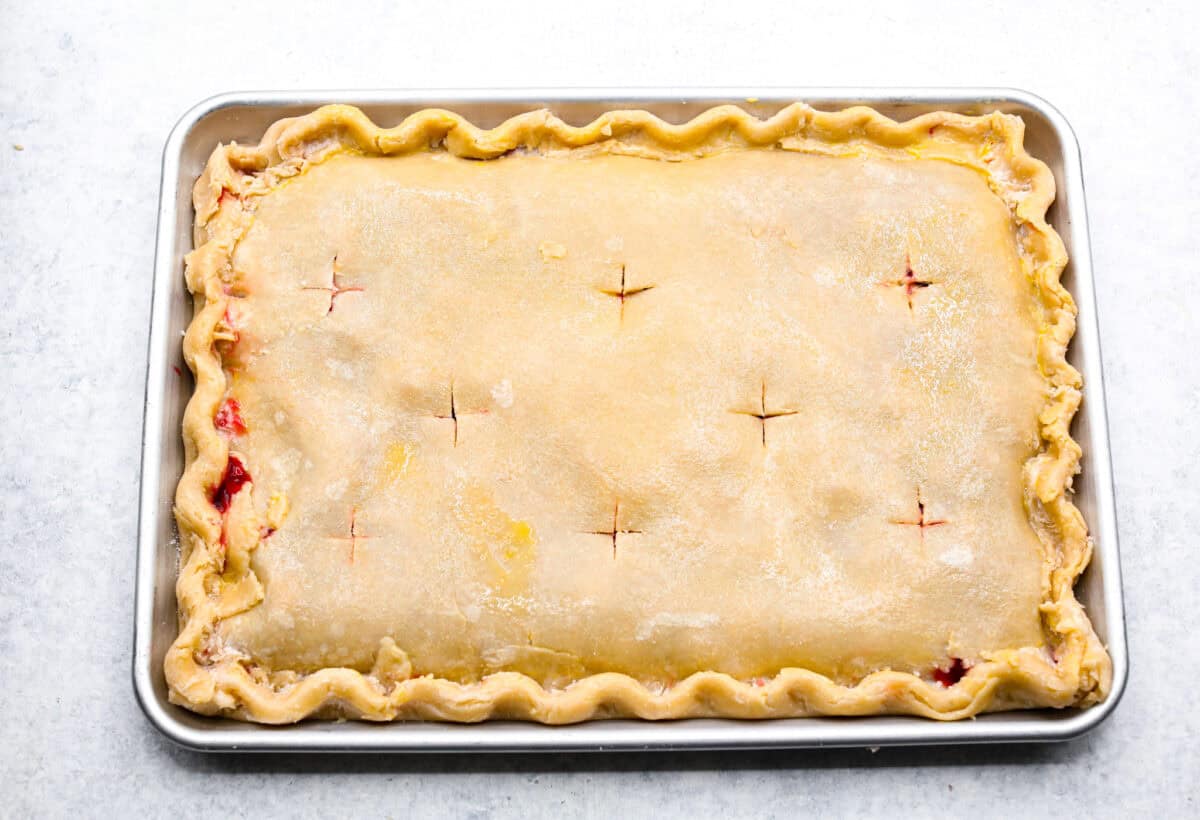 Cherry Slab Pie is an American classic made to serve a crowd! This recipe uses a tender, flaky crust that surrounds sweet, juicy cherry pie filling. It tastes incredibly delicious and is the perfect dessert for any time of year. Overhead shot of cherry slab pie with cross shaped holes cut in to the top crust.