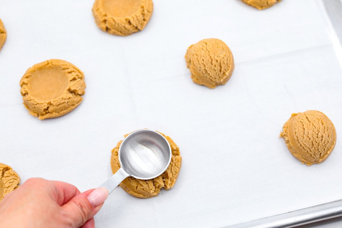 You will absolutely adore these Coffee Cake Cookies! They are loaded with that classic cinnamon sugar flavor, and the crumbly cinnamon streusel is to die for. It’s the perfect treat to enjoy at a special brunch, for the holidays, or a sweet treat for any night of the week. Overhead shot of someone smashing the coffee cake cookie dough balls with the back of a tablespoon.