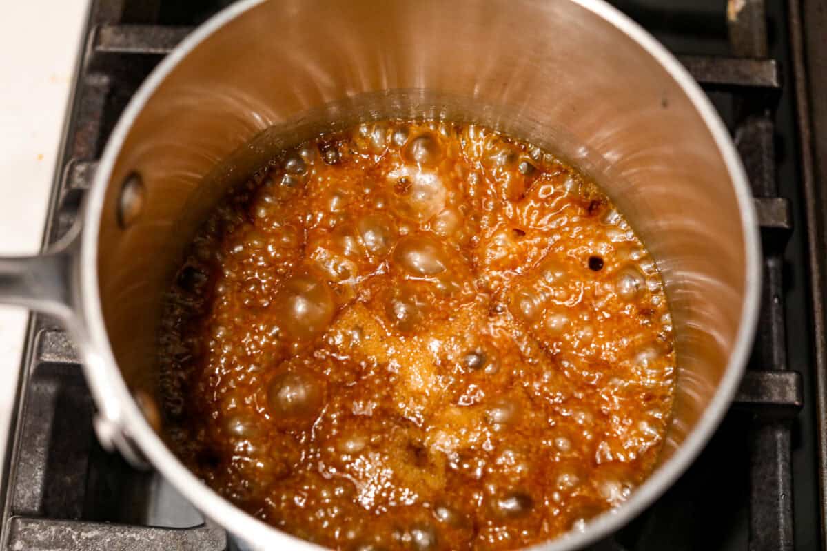 This cornflake brittle crack is crispy, chewy and to die for! With only six ingredients and 8 minutes of prep, you can have this yummy treat ready in no time. This brittle is crunchy cornflakes mixed with a buttery caramel sauce and drizzled in rich dark chocolate. Overhead shot of sugar and butter mixture boiling in a saucepan.