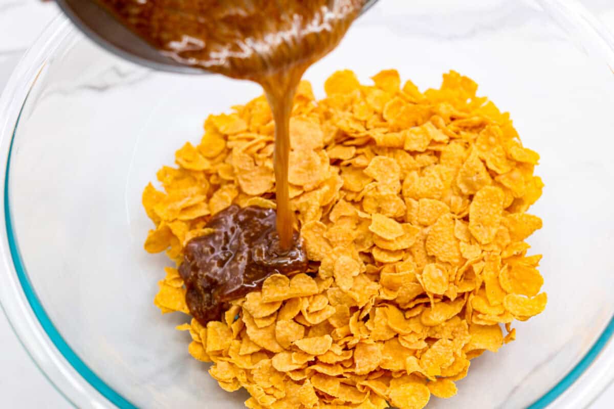 This cornflake brittle crack is crispy, chewy and to die for! With only six ingredients and 8 minutes of prep, you can have this yummy treat ready in no time. This brittle is crunchy cornflakes mixed with a buttery caramel sauce and drizzled in rich dark chocolate. Overhead shot of someone pouring the boiled butter and sugar mixture over a bowl full of cornflakes.