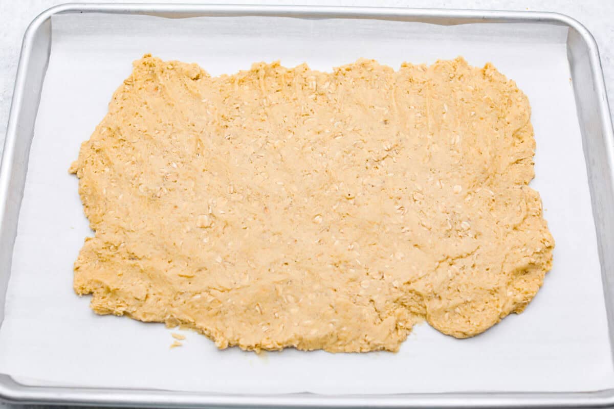 Delicious and addicting, the famous Crack Pie is what made Milk Bar bakery so popular. This copycat recipe is made with a sweet and salty filling tucked inside a crispy oat cookie crust. It’s so good you won’t be able to stop eating it! Overhead shot of oatmeal cookie dough smashed into a rectangle on parchment paper on a cookie sheet.