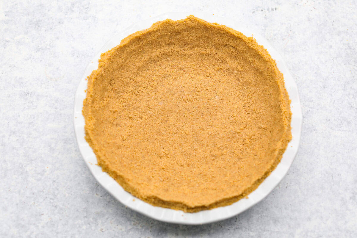 Delicious and addicting, the famous Crack Pie is what made Milk Bar bakery so popular. This copycat recipe is made with a sweet and salty filling tucked inside a crispy oat cookie crust. It’s so good you won’t be able to stop eating it! Overhead shot of crust ingredients smashed into a crust shape in a pie pan.