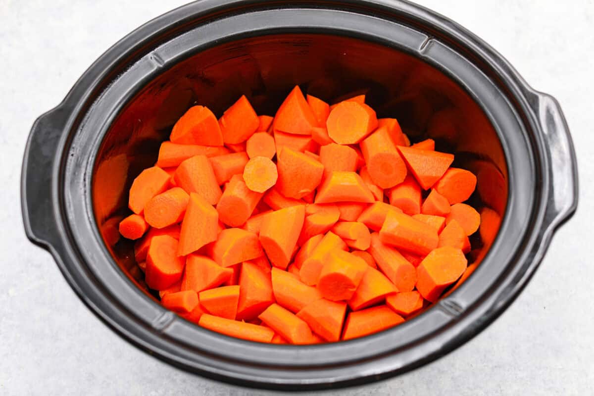 These crockpot carrots will become fork-tender from slowly cooking in your crockpot all day. The carrots have a delicious sweet and savory flavor from the sticky honey and bold garlic, all slathered in butter. They are the perfect side for your next Thanksgiving or Easter feast. Overhead shot of cut up carrots in a crockpot.