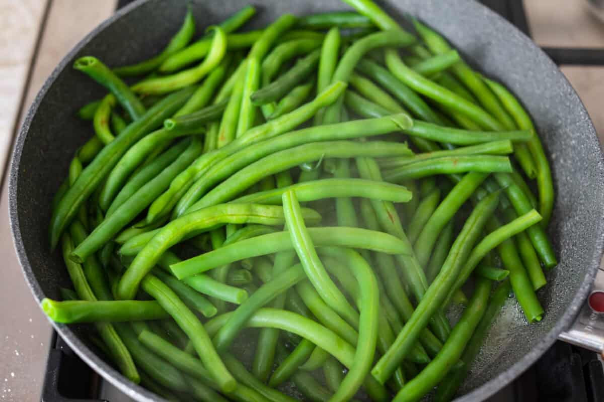 Green Beans Almondine is made with fresh green beans that are sautรฉed until crisp-tender and then tossed with buttery, toasted almonds. Every bite is filled with nutty richness and a hint of lemon to brighten up the flavors. Overhead shot of beans steaming in a skillet.