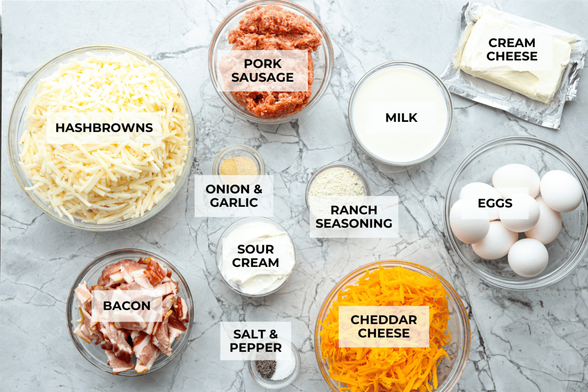 Crack breakfast casserole gets its name for a reason. It is bursting with delicious flavors you won't want to stop eating! It's packed with layers of shredded potatoes, crispy bacon, sausage, and smooth cream cheese, topped with a layer of crispy cheese. Overhead shot of labeled ingredients.