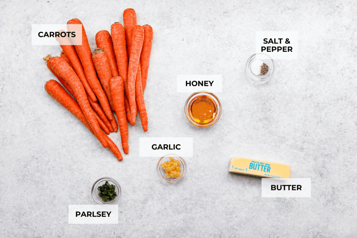 These crockpot carrots will become fork-tender from slowly cooking in your crockpot all day. The carrots have a delicious sweet and savory flavor from the sticky honey and bold garlic, all slathered in butter. They are the perfect side for your next Thanksgiving or Easter feast. Overhead shot of labeled ingredients.