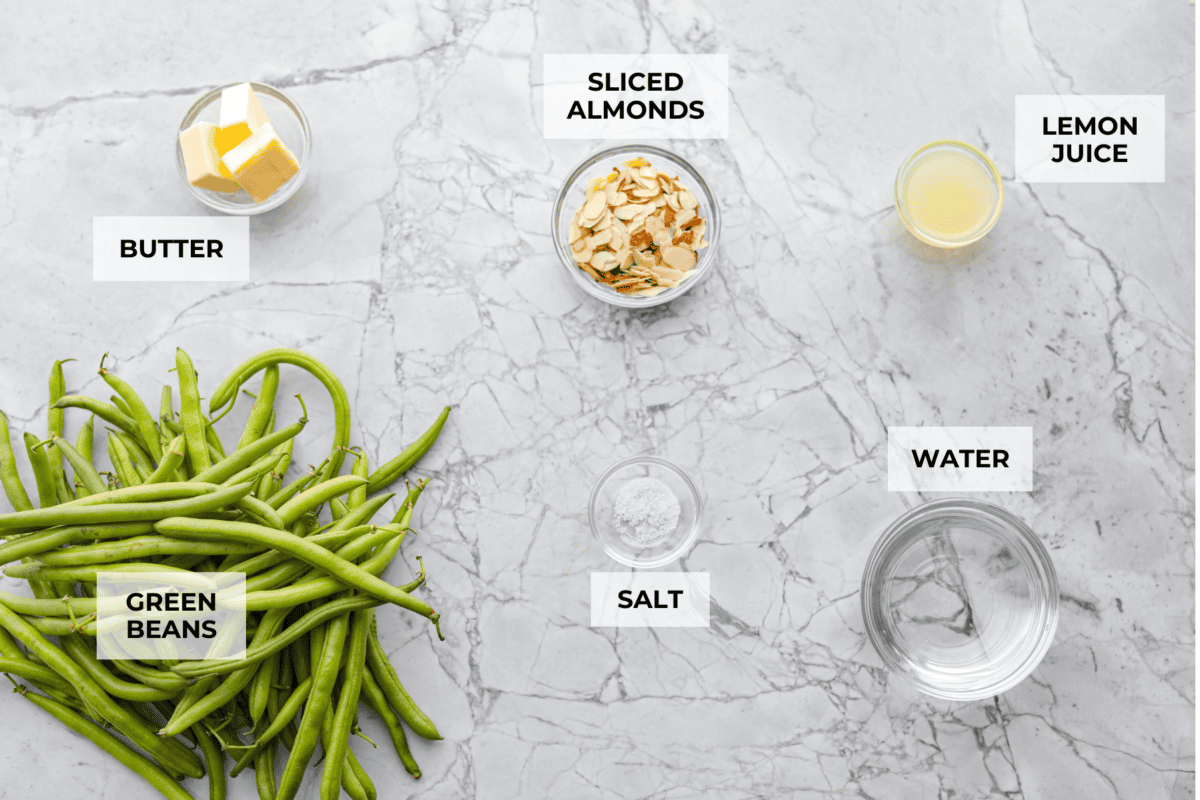 Green Beans Almondine is made with fresh green beans that are sautรฉed until crisp-tender and then tossed with buttery, toasted almonds. Every bite is filled with nutty richness and a hint of lemon to brighten up the flavors. Overhead shot of labeled ingredients.