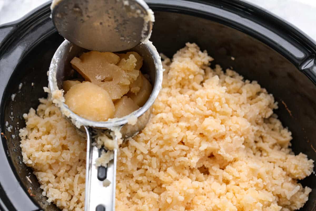 Million dollar mashed potatoes are unmatched when it comes to creamy velvety mashed potatoes. They get their intense flavors and smooth texture from letting the potatoes slow cook in chicken broth then mixing them with cream cheese, butter and garlic. Overhead shot of someone mashing potatoes into the crock pot.