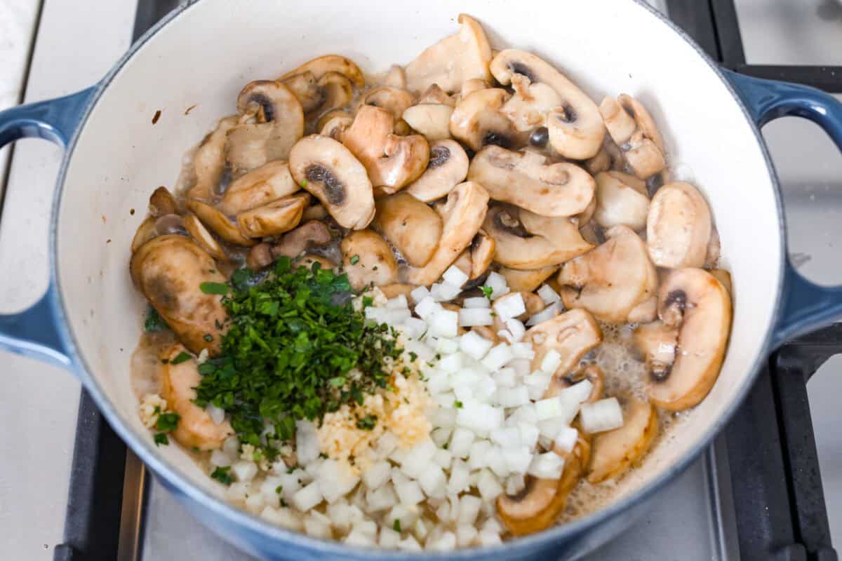 Mushroom bisque is full of cream and garlic-infused mushrooms, all blended to make a thick, rich, and beyond flavorful soup! You will want to drink this straight from your bowl! Overhead shot of sautéing mushrooms with herbs, onions and seasonings added.