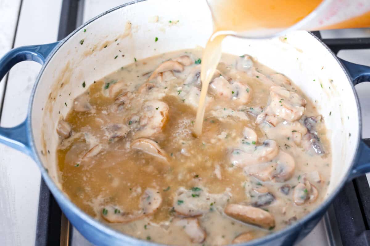 Mushroom bisque is full of cream and garlic-infused mushrooms, all blended to make a thick, rich, and beyond flavorful soup! You will want to drink this straight from your bowl! Angle shot of broth being poured into the mushroom and flour mixture.