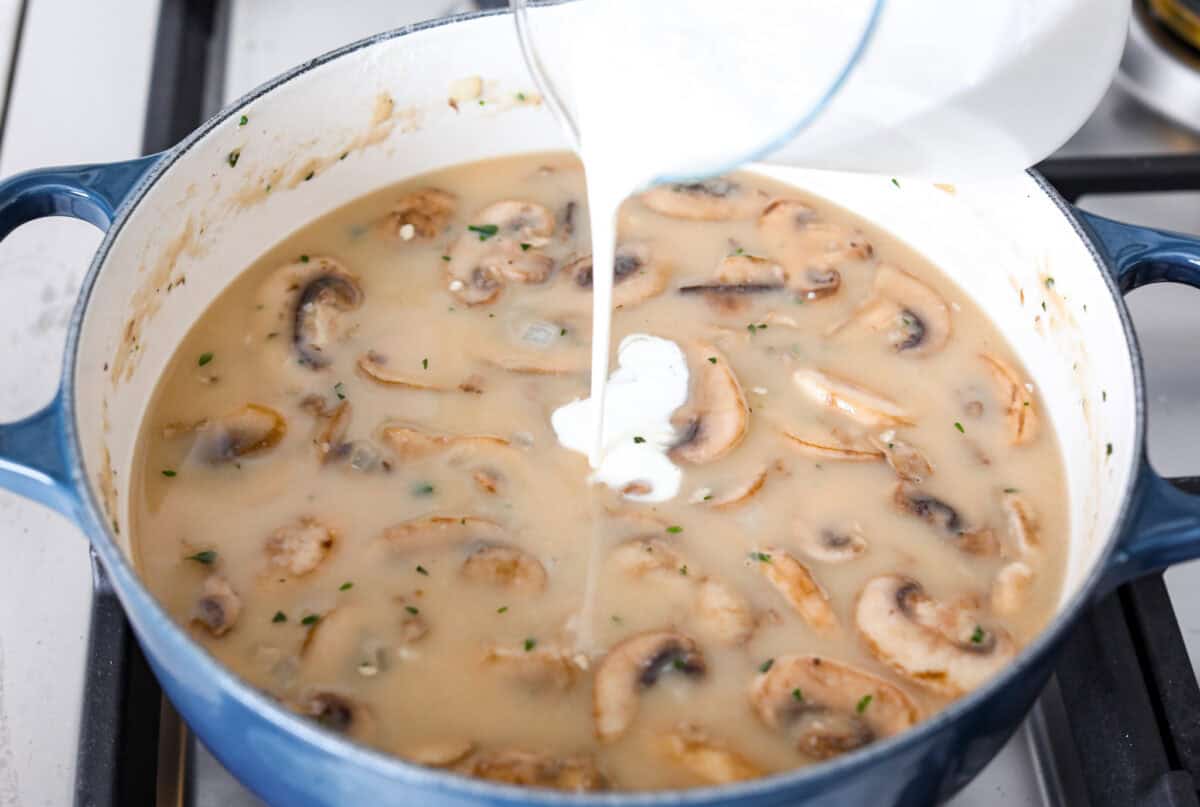 Mushroom bisque is full of cream and garlic-infused mushrooms, all blended to make a thick, rich, and beyond flavorful soup! You will want to drink this straight from your bowl! Angle shot of cream being poured into the mushroom, flour and broth mixture.