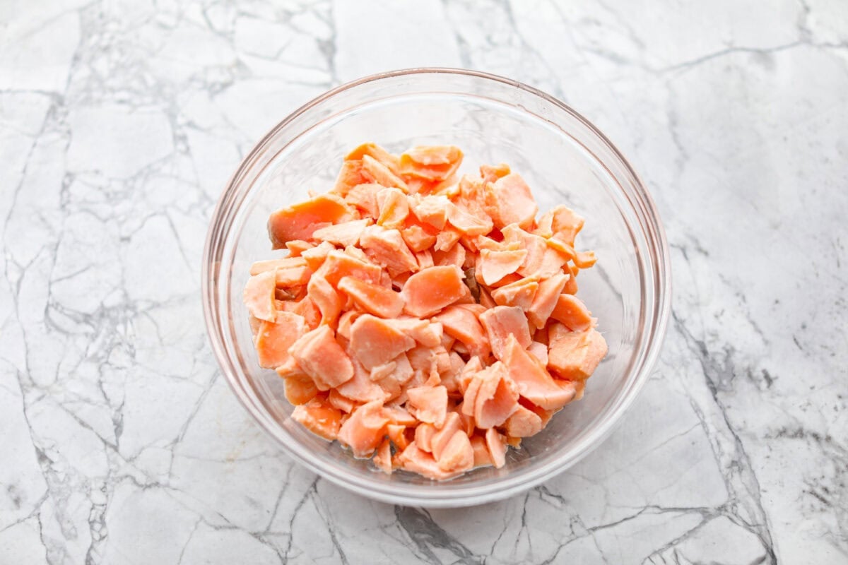 Salmon rillettes is a creamy, flavorful spread made with fresh and smoked salmon blended with lemon, sour cream, and herbs. It is perfect for spreading on crackers or toasted baguette slices. This elegant appetizer is a crowd-pleaser for any occasion! Overhead shot of flaked salmon in a glass bowl.