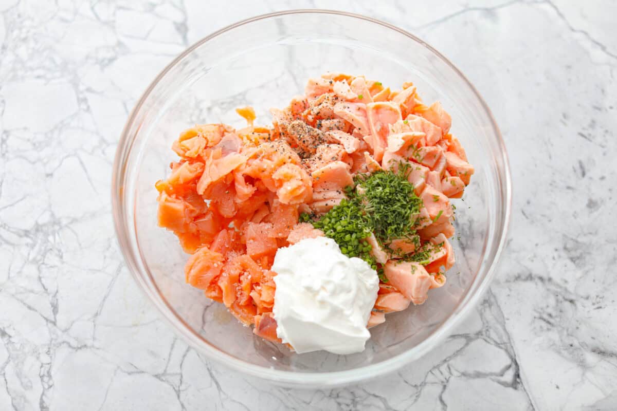 Salmon rillettes is a creamy, flavorful spread made with fresh and smoked salmon blended with lemon, sour cream, and herbs. It is perfect for spreading on crackers or toasted baguette slices. This elegant appetizer is a crowd-pleaser for any occasion! Overhead shot of flaked and smoked salmon mixed with herbs, lemon juice and sour cream.