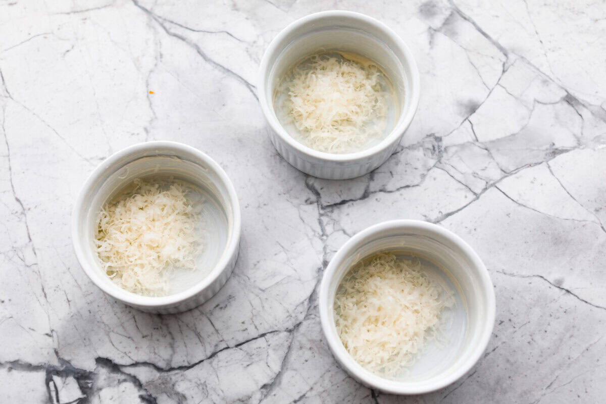 Shirred Eggs are a breakfast worth waking up for in the morning! They're a creamy, custardy combination of eggs, cheese, cream, and bacon that bake in individual ramekins. It's a simple yet super tasty way to start the day! Overhead shot of three ramekins with cheese in the bottom.