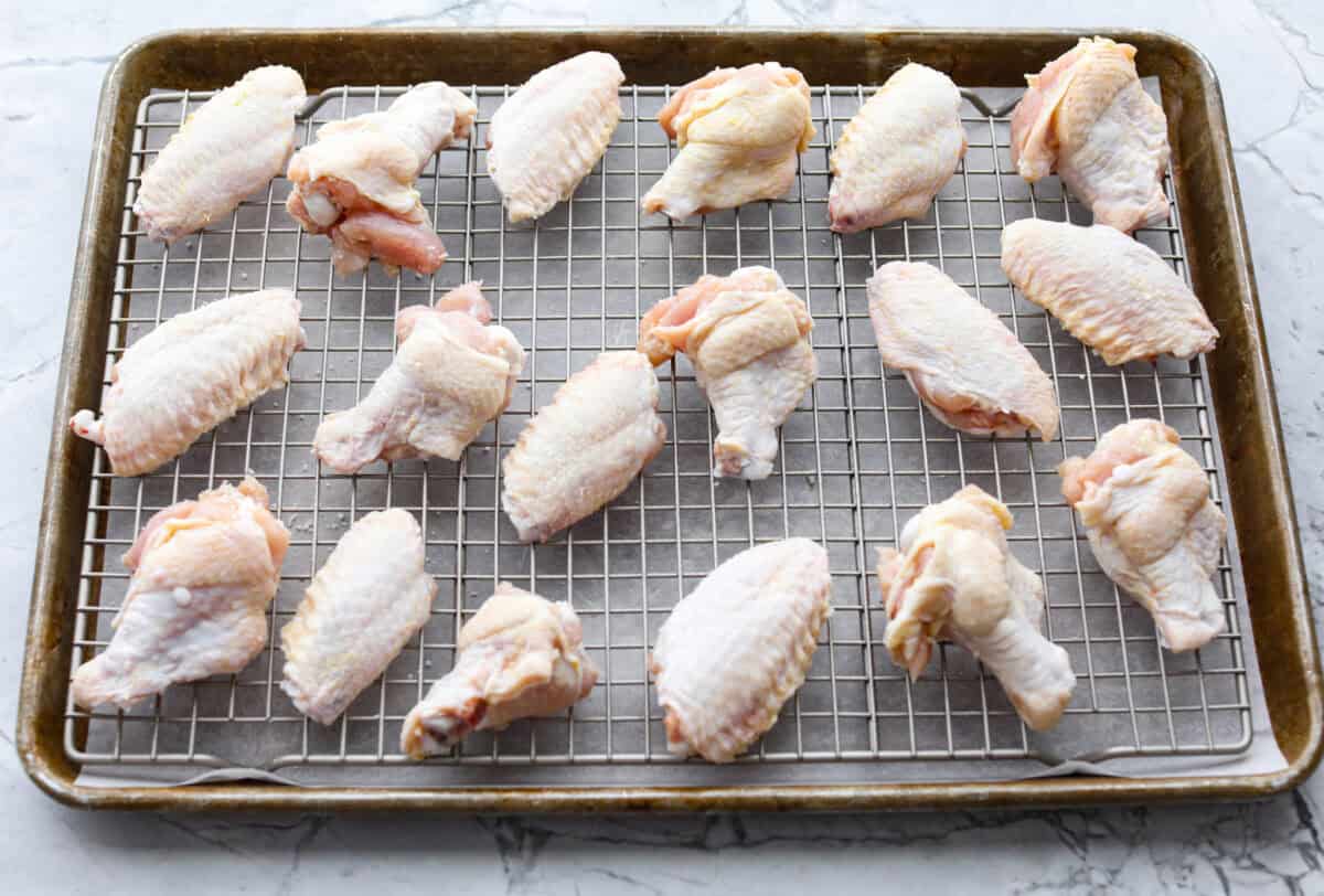 These sweet and sour wings are the perfect appetizer to serve for your next party, game day, or after-school snack. They are baked to crispy perfection and then doused in a sticky, sweet, and sour sauce. Raw wings on a baking rack over parchment paper on a cookie sheet.