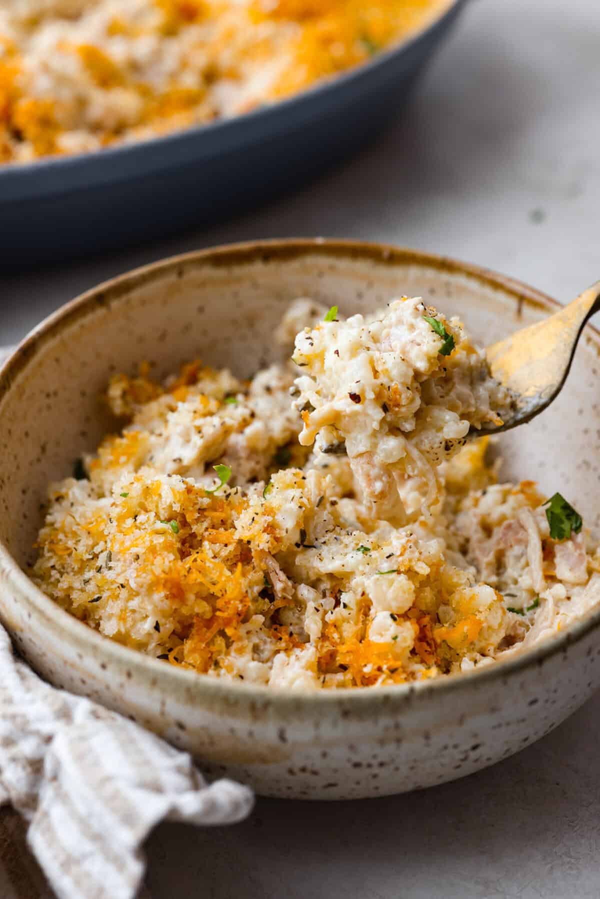 Angel Chicken and Rice Casserole is a creamy, cheesy, comforting classic. Tender chicken is folded into fluffy rice smothered in a savory cream sauce. The top has the most perfectly toasty cheesy crunch. You're going to love it! Angle shot of a bowl of angel chicken and rice casserole.