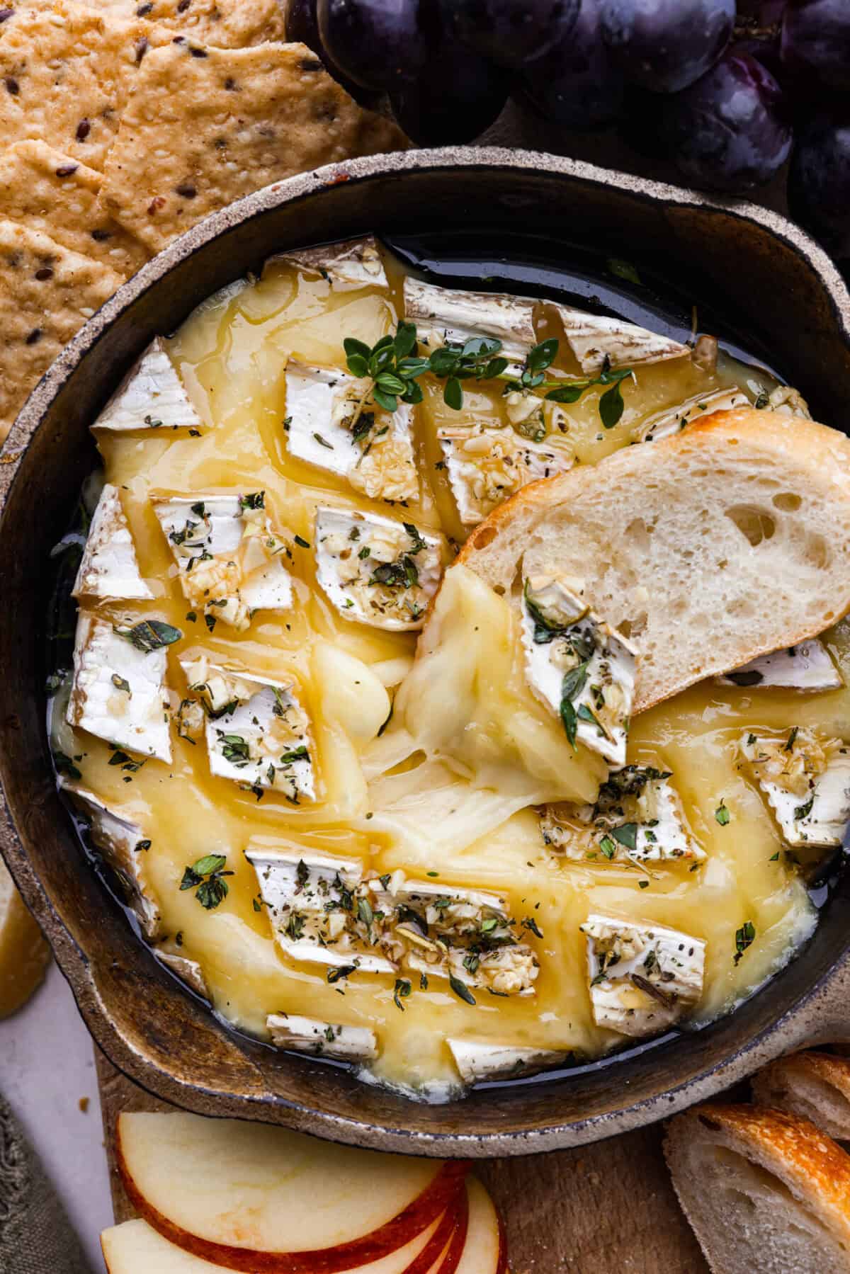 Warm and gooey baked brie is a hit for any occasion! With just five simple ingredients and less than 20 minutes, you will have a rich, creamy appetizer that's impossible to resist. Scoop it up with your favorite crackers or bread! Overhead shot of melty baked brie in a skillet with pice of bread in it.
